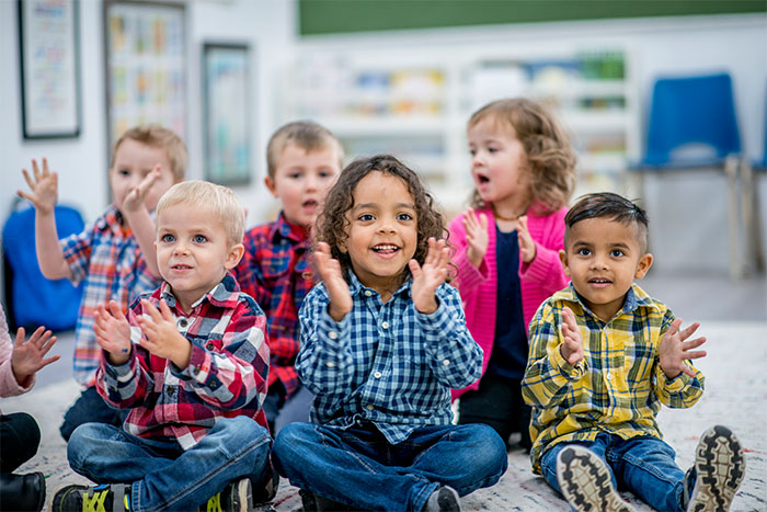Mehrere fröhliche Kindergartenkinder sitzen auf dem Boden und klatschen in die Hände.