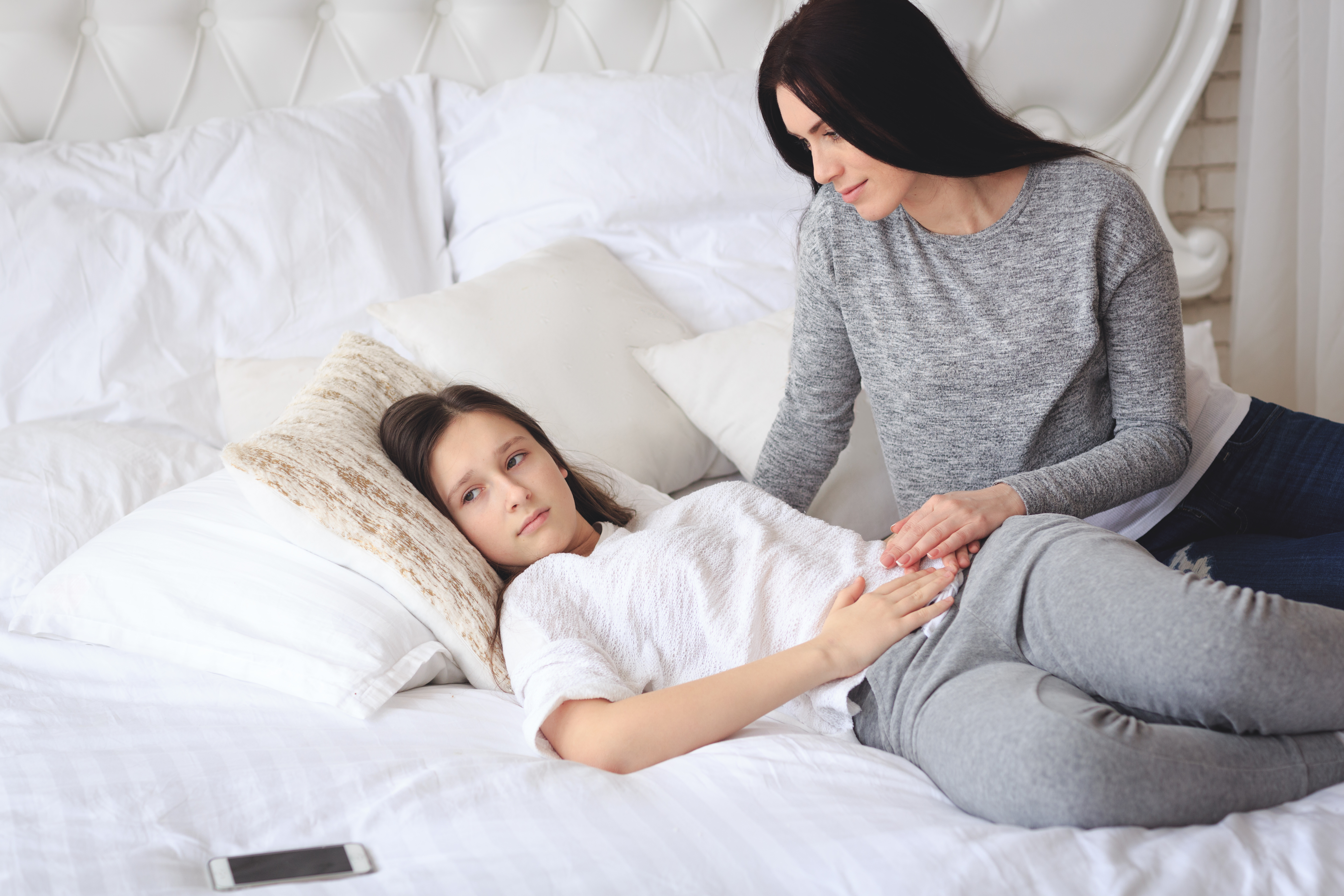 Mutter unterstützt ihre besorgte Tochter, die mit Regelschmerzen im Bett liegt — Erfahrungsbericht zu Regelblutungen bei einer Konduktorin mit Hämophilie A